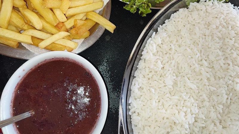 Prato com molho escuro de juçara, arroz e batata frita no restaurante Sabores do Quilombo, em Ubatuba