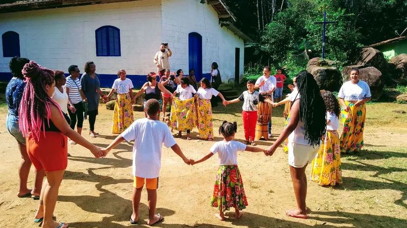 Roda de ciranda com crianças e adultos da comunidade em frente a uma casa no Quilombo da Fazenda