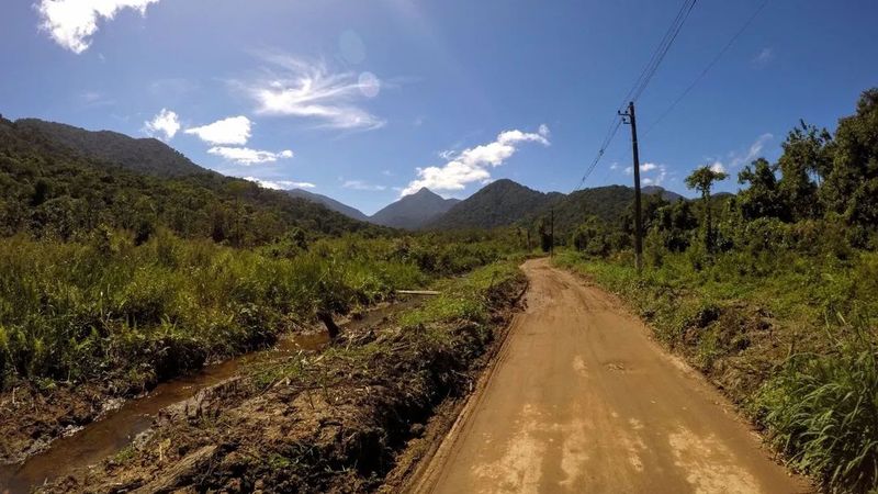 Estrada de terra entre a mata e o campo, com as montanhas da Serra do Mar ao fundo, no caminho do Quilombo da Fazenda